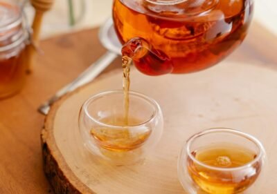 Aesthetic pouring of herbal tea into glass teacups with honey and flowers in a cozy indoor setting.