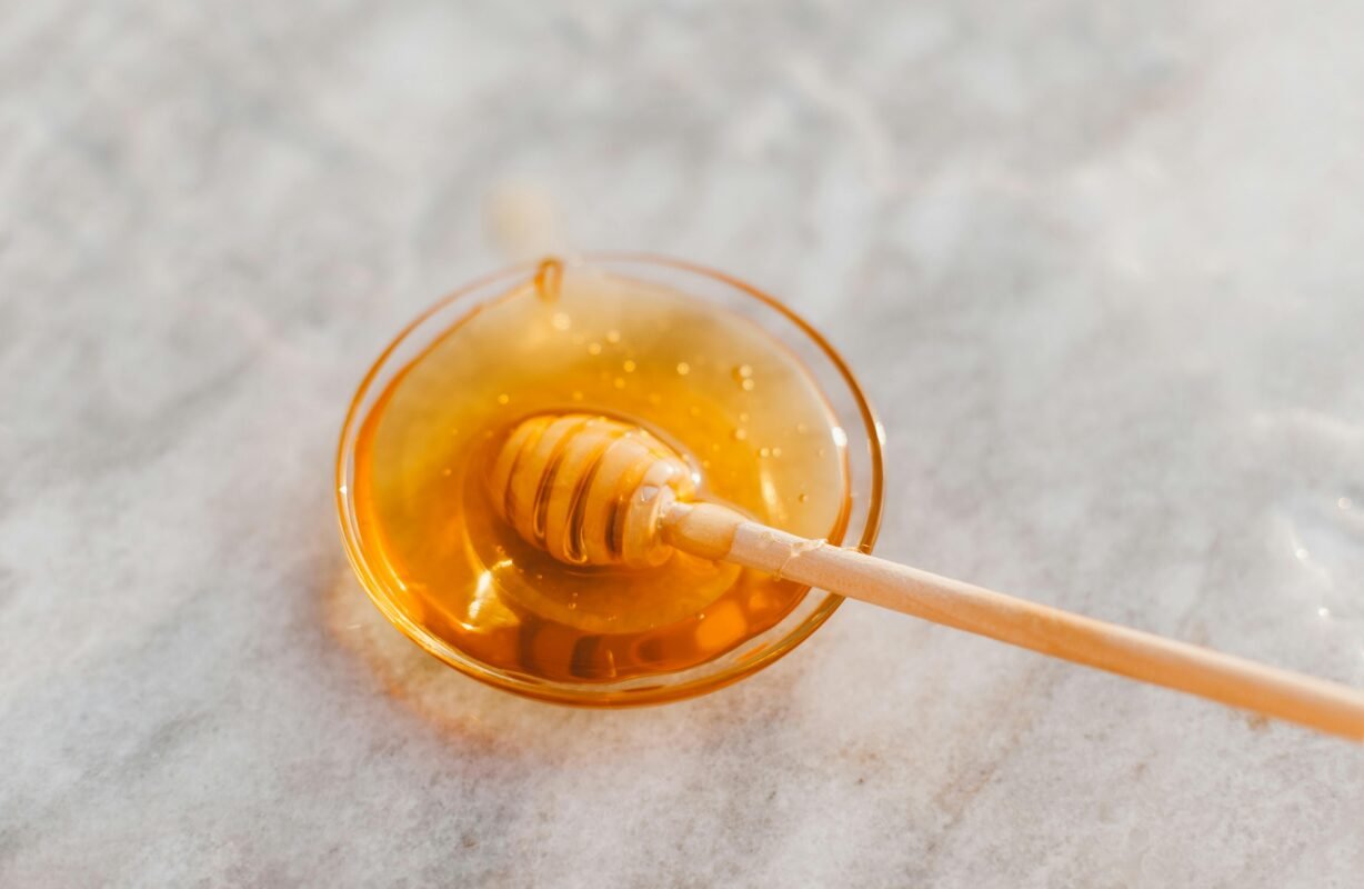 A close-up shot of a honey dripper resting in a glass bowl filled with golden honey.